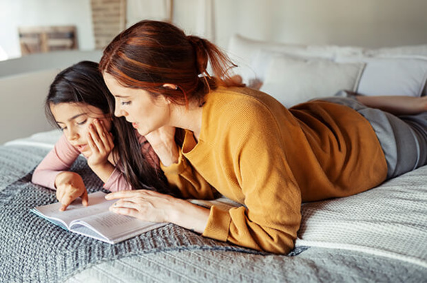 Mutter und Tochter lesen zusammen auf Bett